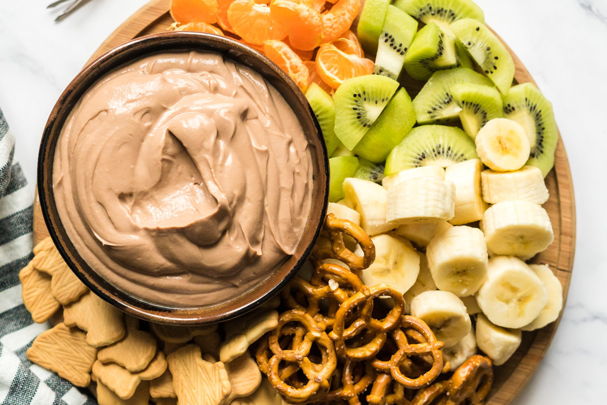 nutella yogurt dip surrounded by mandarin orange slices, kiwi slices, banana slices, pretzels, and animal crackers